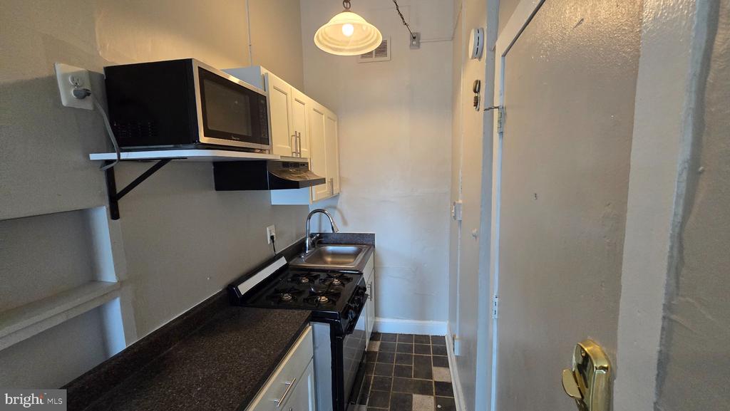 Narrow galley kitchen with dark countertops, white cabinets, and a black gas range and microwave.
