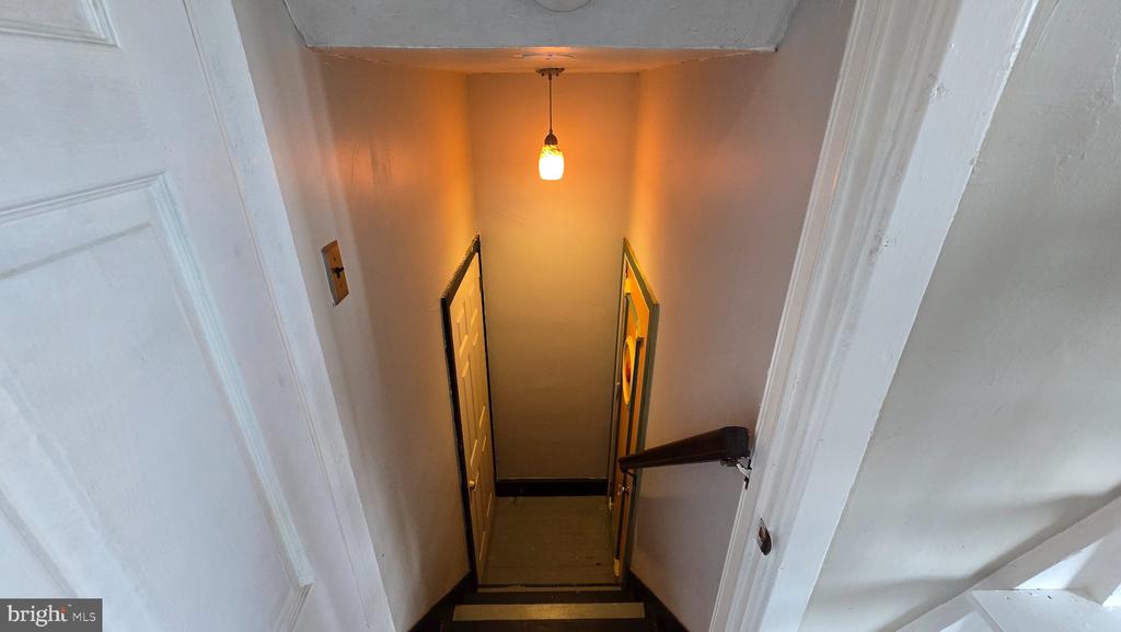 Narrow stairwell descending to a landing beneath a warm pendant light.