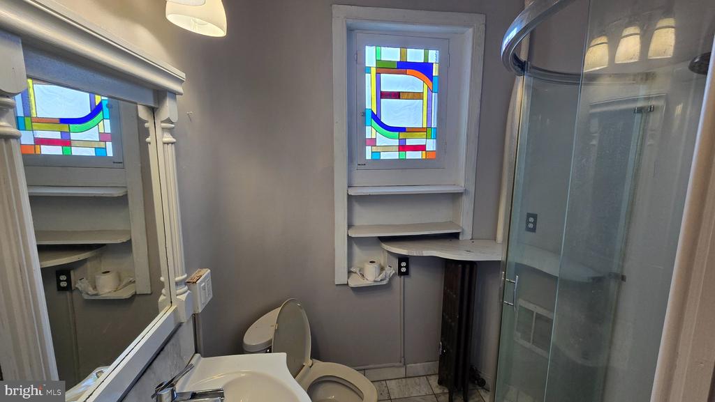 Bathroom with colorful stained-glass windows, a sink, toilet, and glass-enclosed shower.