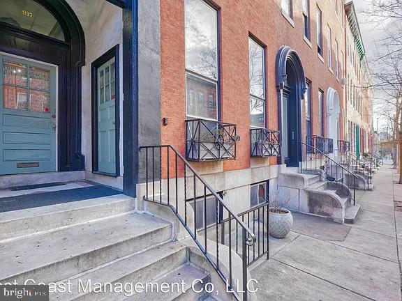Brick rowhouse entrances with blue doors, raised concrete stoops, and black iron railings.