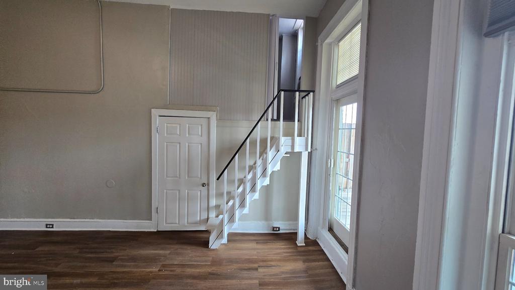 Vacant room with a staircase, dark hardwood floors, and tall windows.