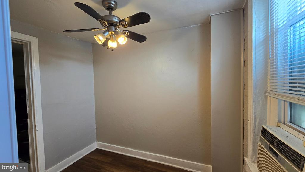 Vacant room with dark wood floors, a lit ceiling fan, and a window air conditioner.
