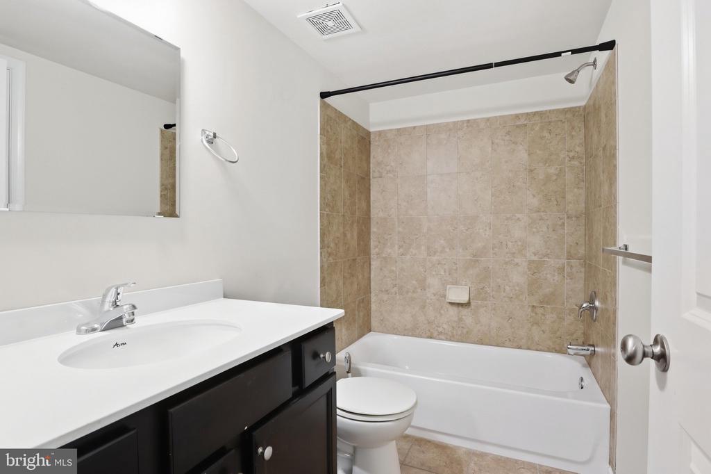 Bathroom with beige tile around the bathtub and a dark vanity with a white sink.