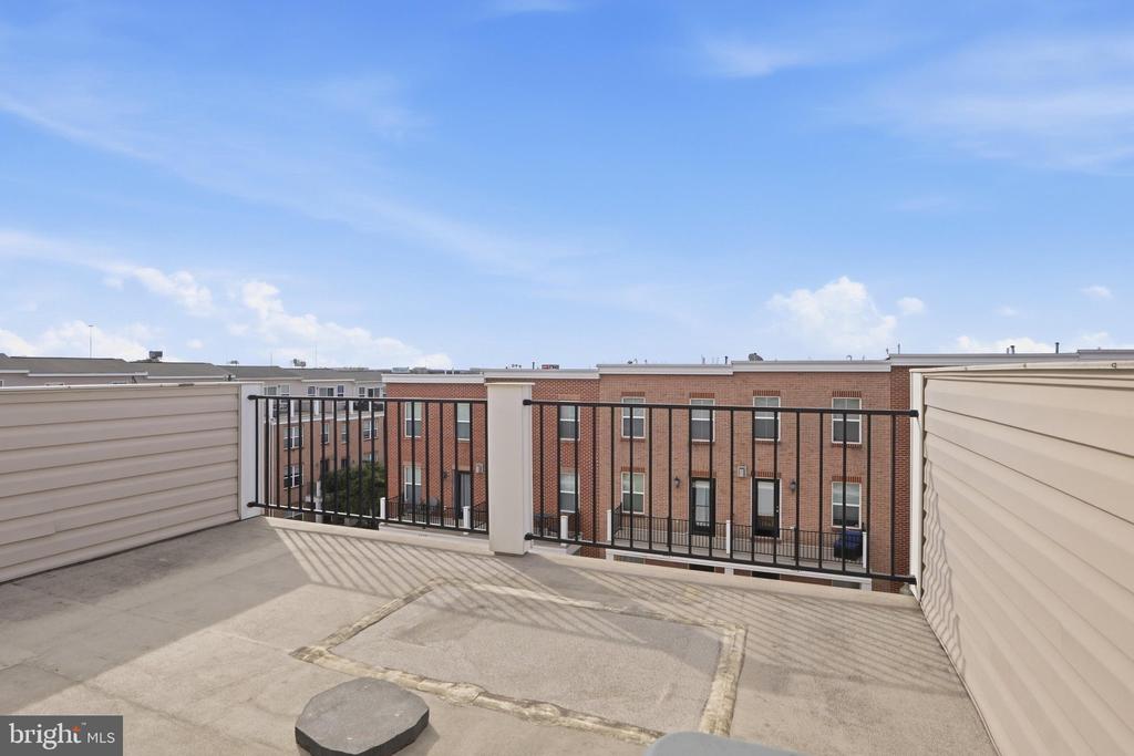 Rooftop terrace with black railing overlooking neighboring brick townhouses.