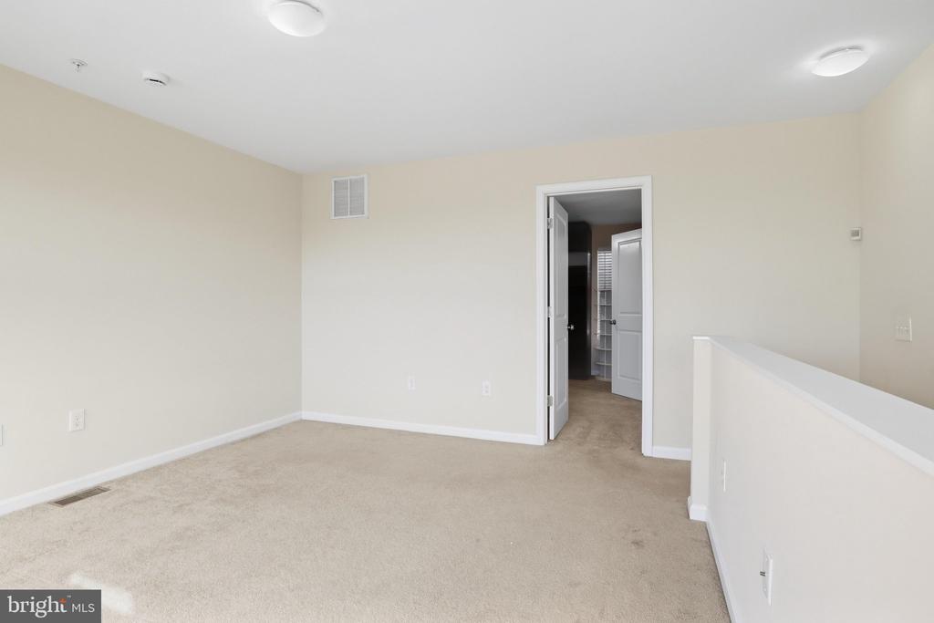 Empty carpeted room with an open doorway and white half-wall railing.