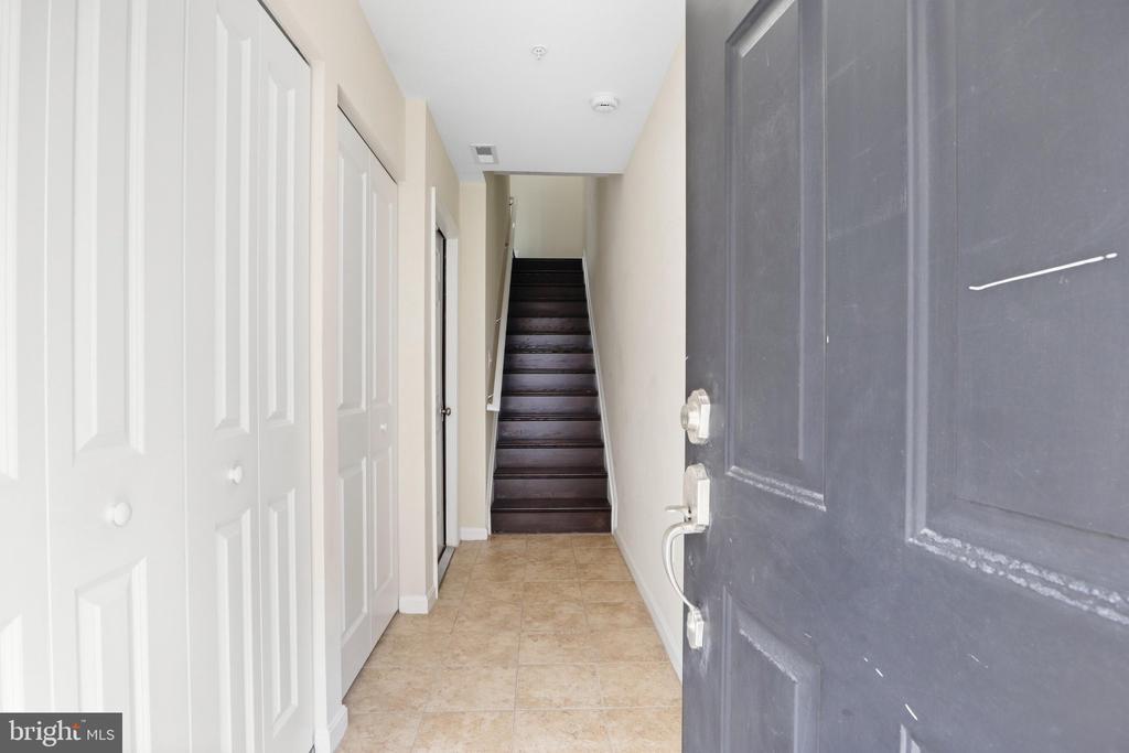 Entry hallway with white closet doors, beige tile, and a staircase at the far end.