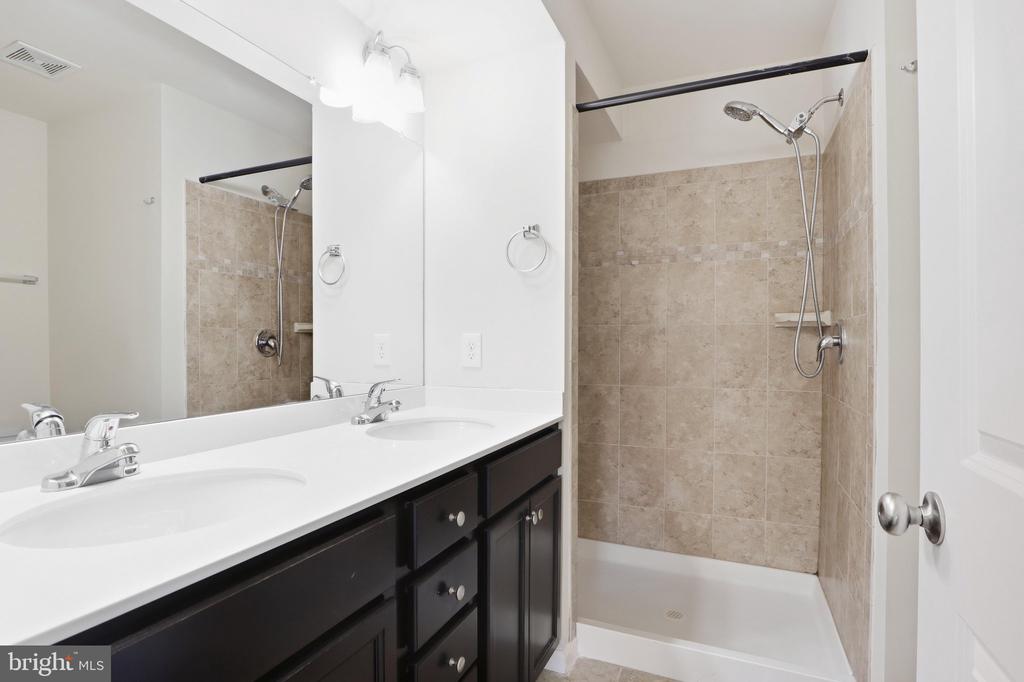 Bathroom with a white double-sink vanity and beige tiled shower.