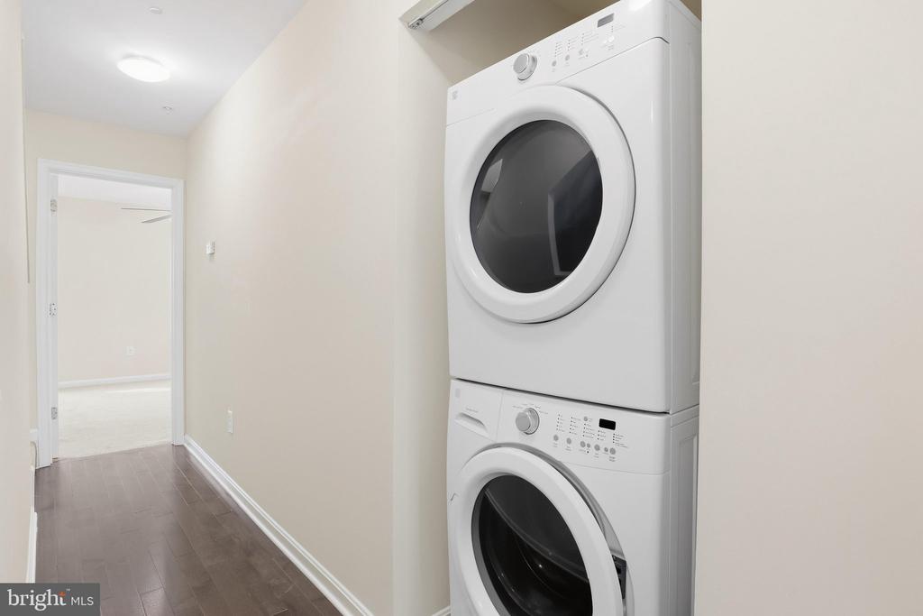 Laundry hallway with a stacked white washer and dryer and dark wood flooring.