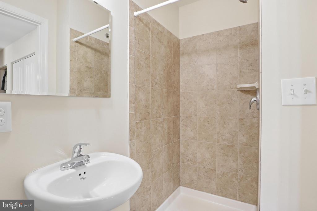 Bathroom with a white sink and mirror beside a beige-tiled shower.