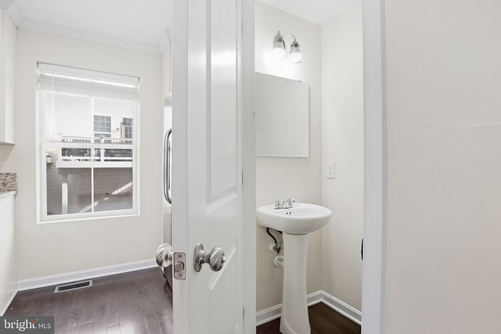 Bathroom with a white pedestal sink, wall mirror, and window overlooking neighboring buildings.