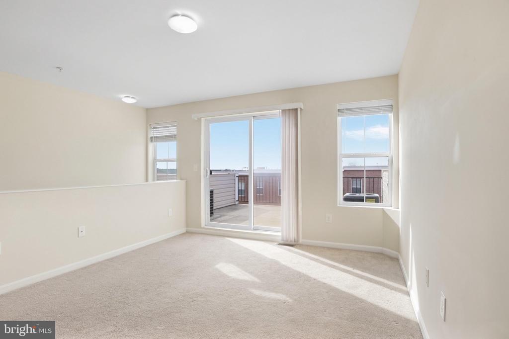 Carpeted room with a sliding glass door to a balcony and two windows.