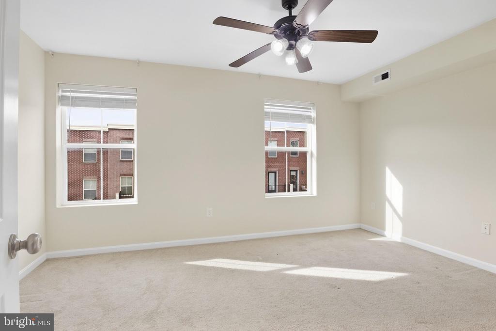 Vacant carpeted bedroom with two windows and a ceiling fan.