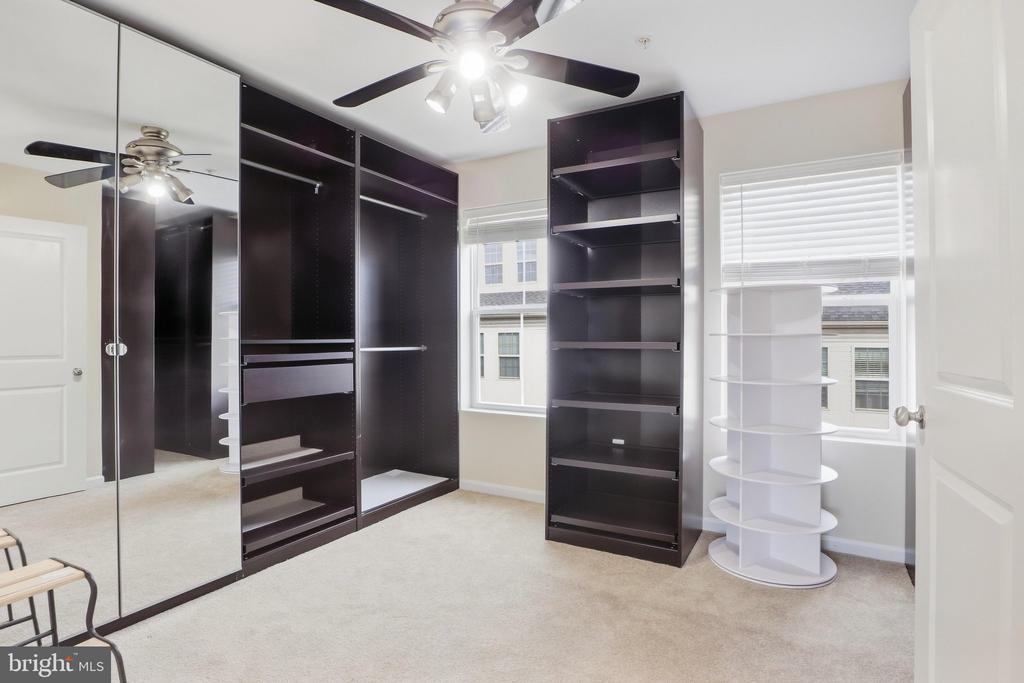 Walk-in closet with mirrored doors, dark built-in shelving, and a white rotating display shelf.