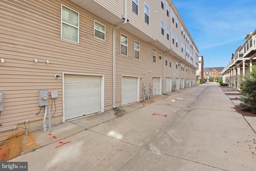 Townhome row with tan siding and garage doors lining a shared concrete driveway.