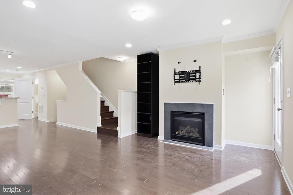 Empty living room with dark wood floors, a fireplace, black shelving, and stairs.