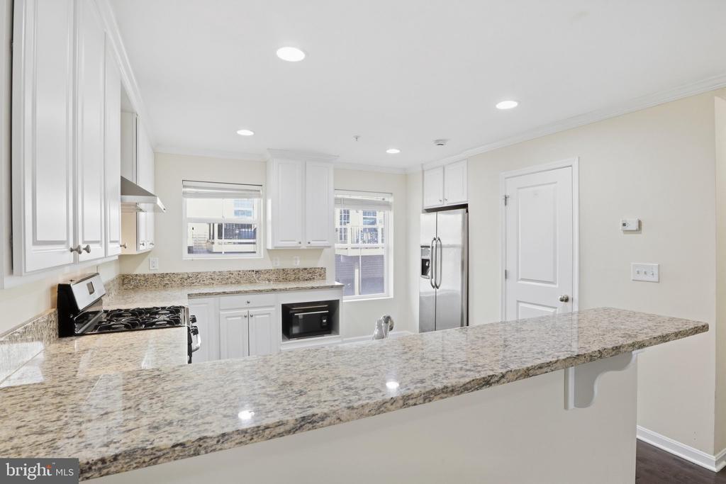Kitchen with white cabinets, granite counters, a long breakfast bar and stainless-steel refrigerator.