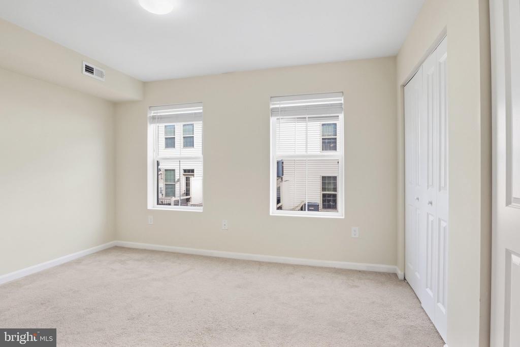 Empty bedroom with two windows, light carpet, and a white double-door closet.