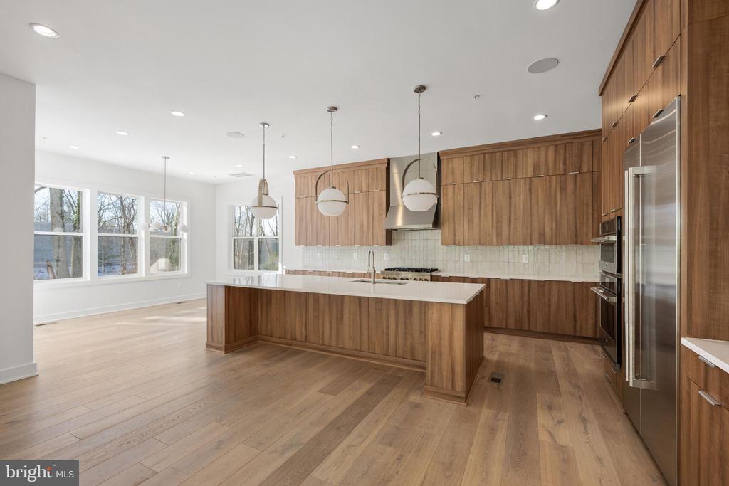 Vacant kitchen with a large white island, warm wood cabinetry, and wide windows.
