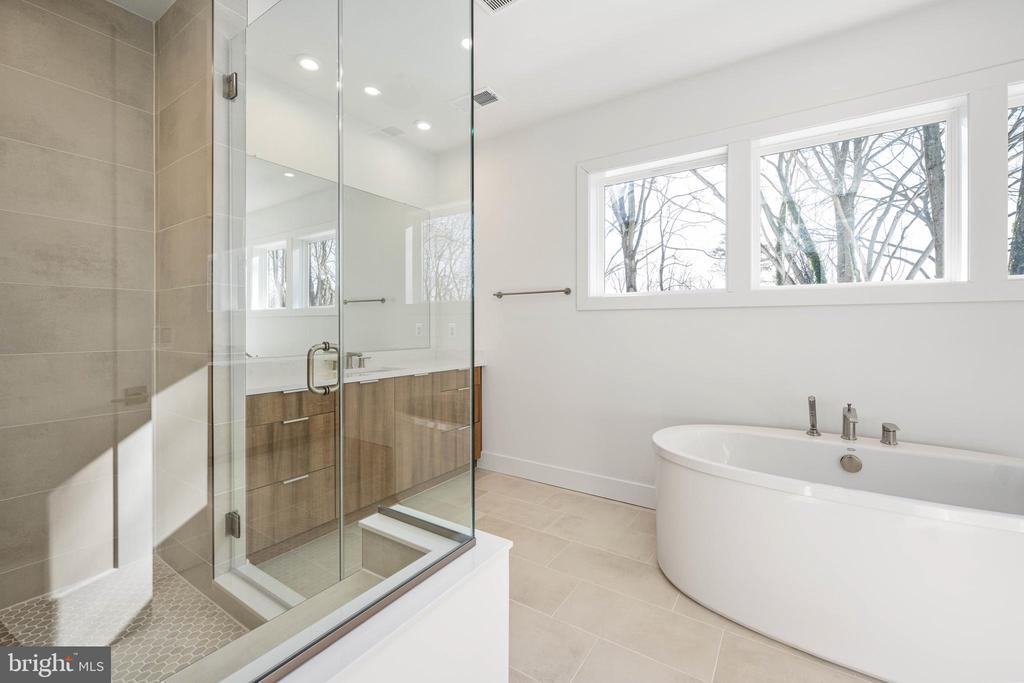 Modern bathroom with a glass shower, freestanding tub, and wide windows overlooking trees.
