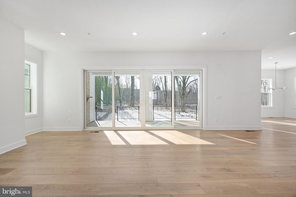 Vacant living area with pale wood floors and wide sliding glass doors overlooking trees.