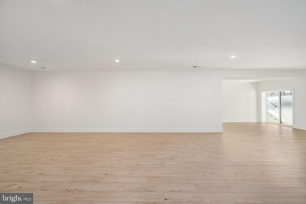 Vacant room with light wood floors, recessed lights, and sliding glass doors beside a stairway.