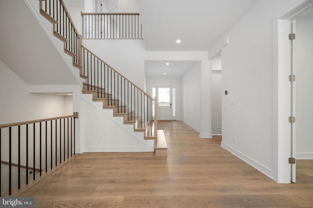 Vacant entry hall with light wood floors and an open staircase with dark metal balusters.