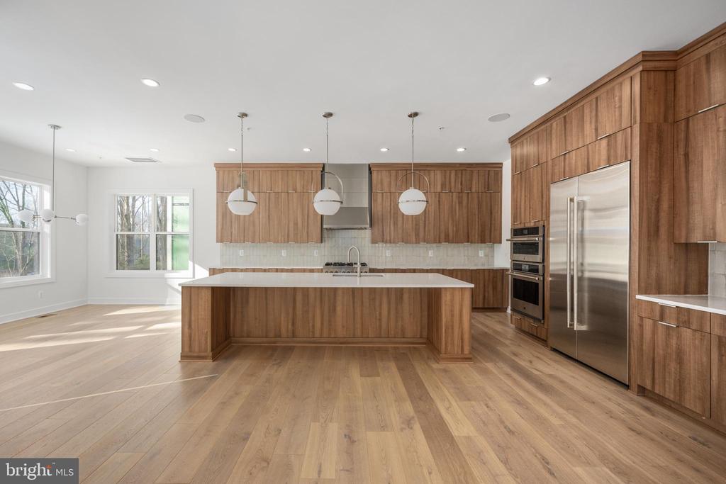 Modern kitchen with wood cabinetry, a large island, and stainless steel appliances.