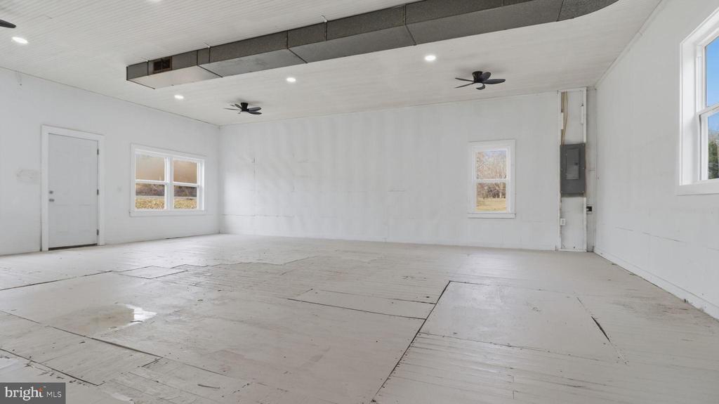 Large empty room with a worn panelled floor, several windows, and two ceiling fans.