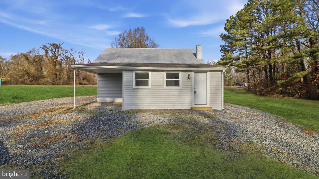 Small gray-sided home with a gravel driveway, covered carport, and lawn.