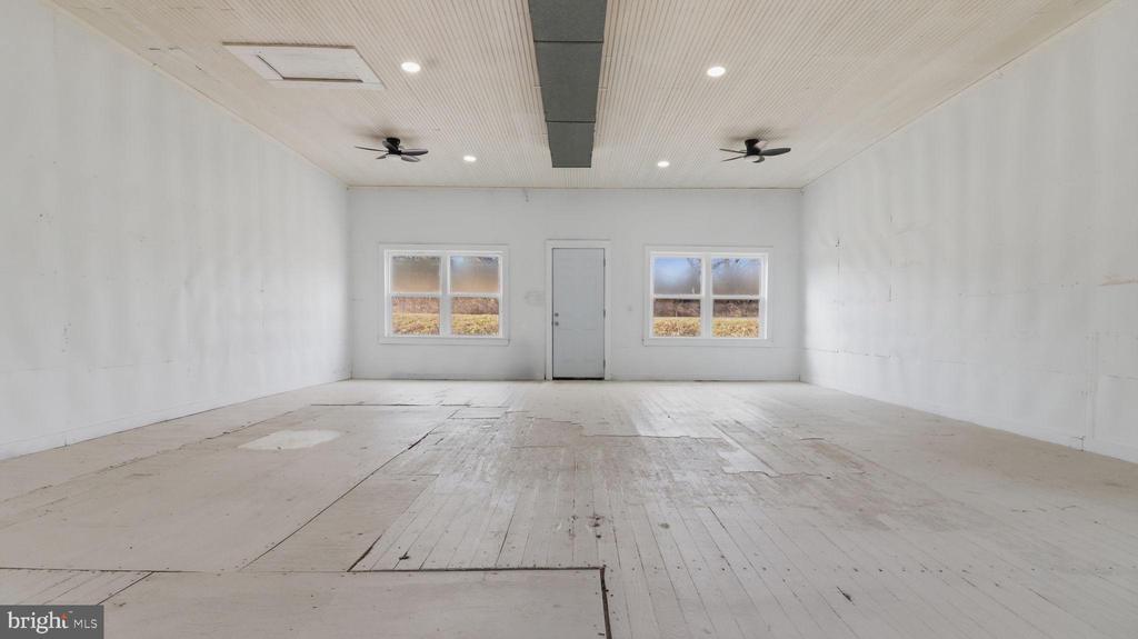 Empty white room with a worn plank floor, two ceiling fans, and windows beside the far door.