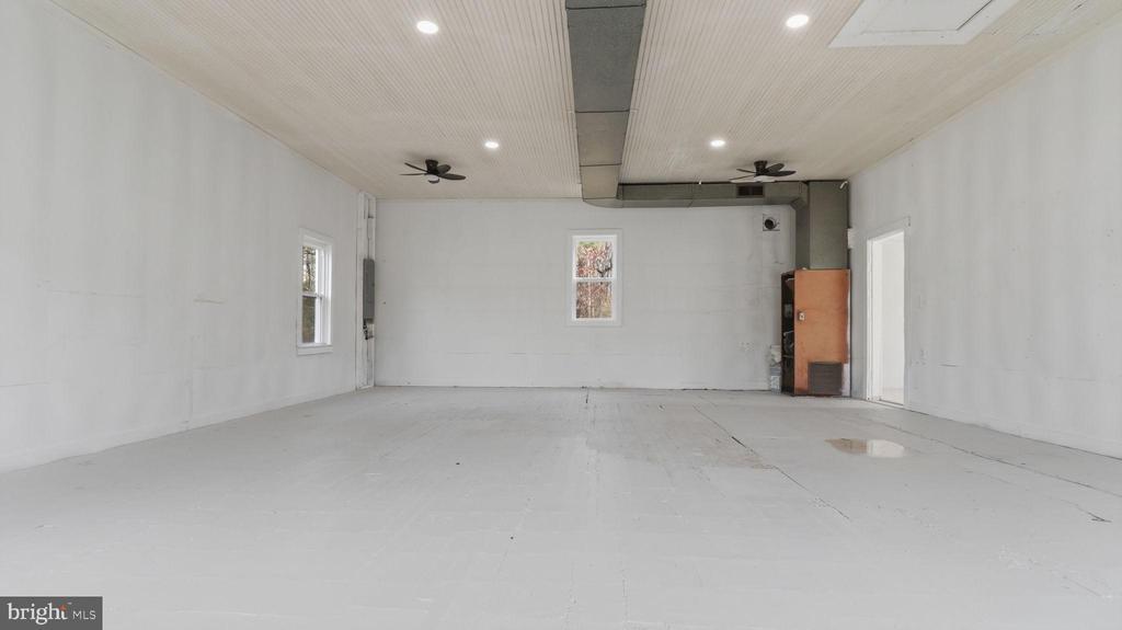Empty garage with a broad light-colored floor, several windows, ceiling fans, and exposed overhead ductwork.