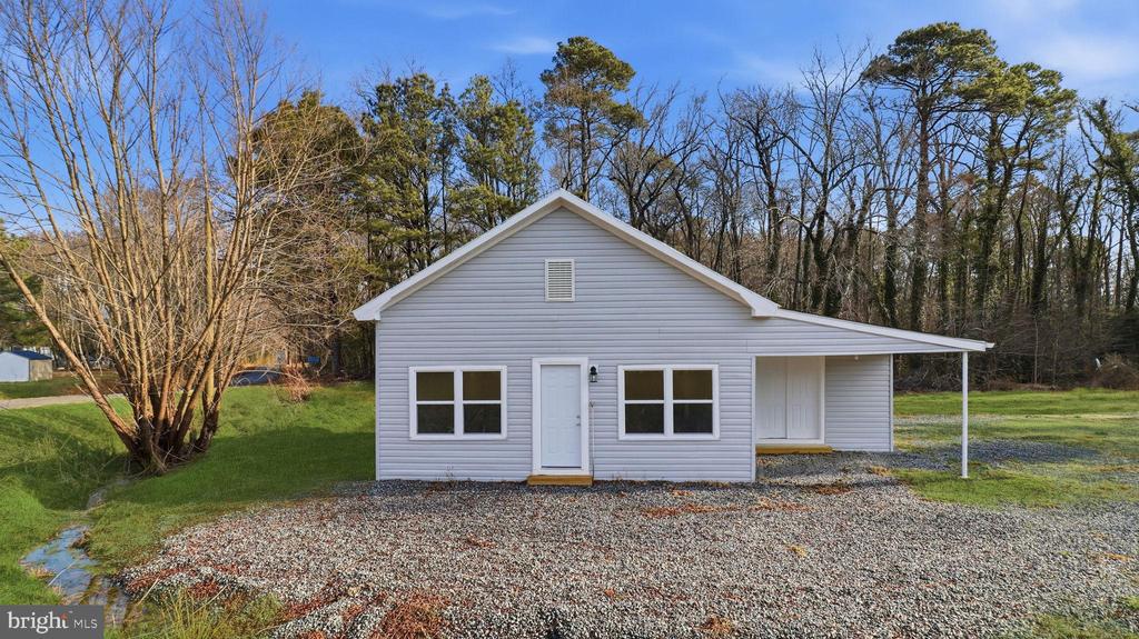 Light-gray single-story home with white trim, a gravel driveway, and a covered side carport.