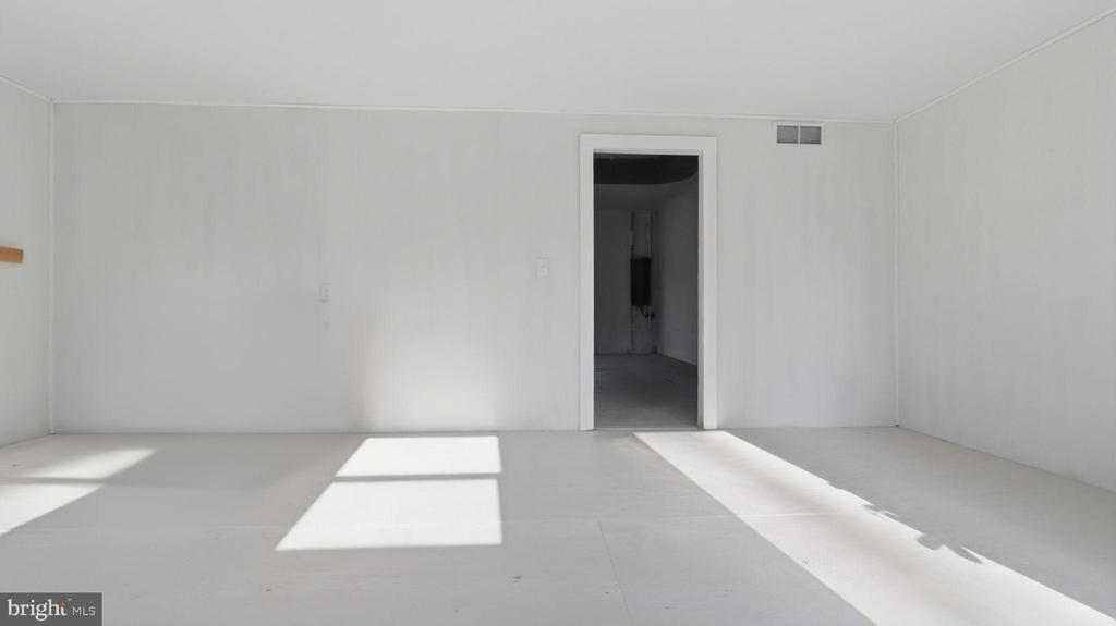 Vacant white room with sunlight across the floor and an open doorway to a darker adjoining space.