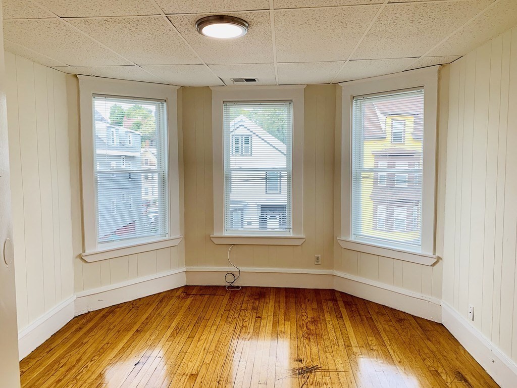 Vacant room with three tall windows and glossy hardwood floors.
