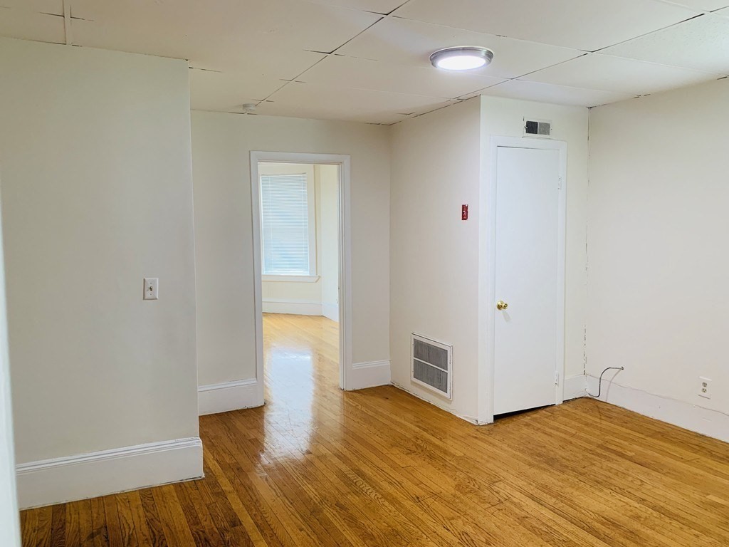 Empty room with hardwood floors and a doorway to a brighter room with a window.