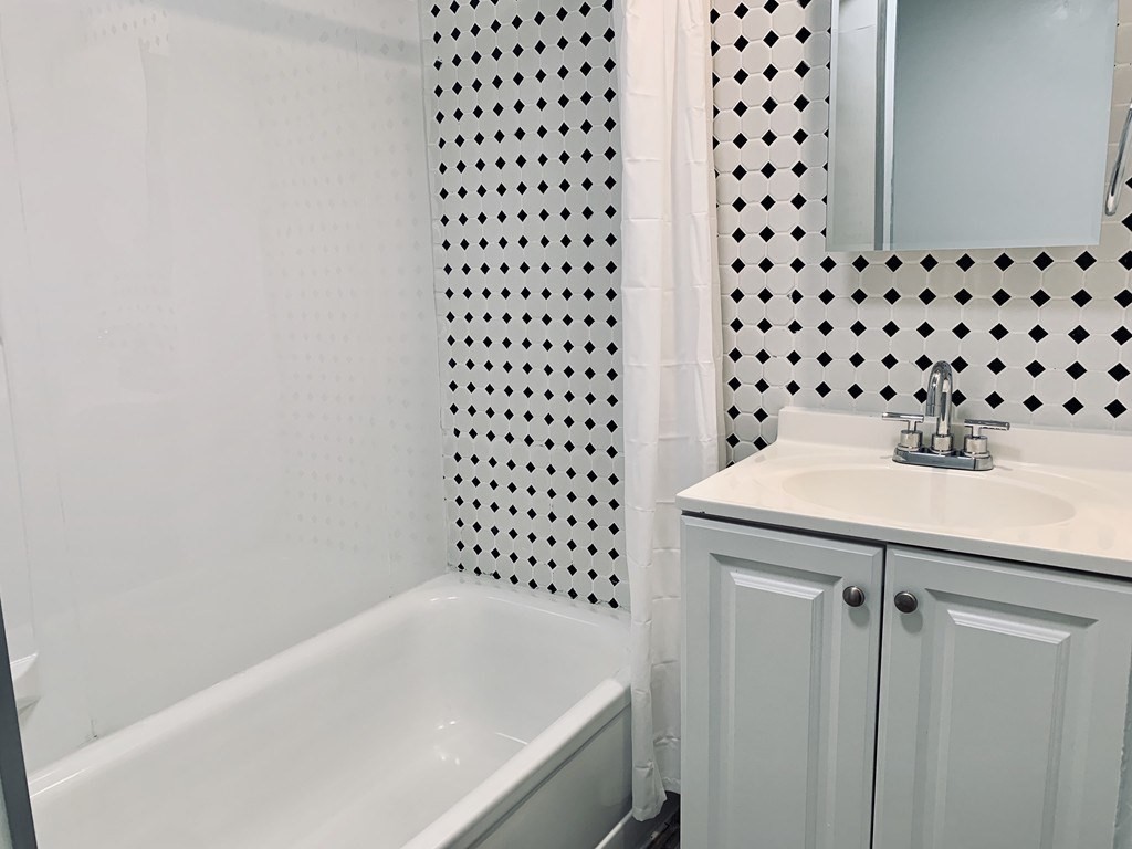 Bathroom with a white bathtub, black diamond-patterned wall tiles, and a white vanity.