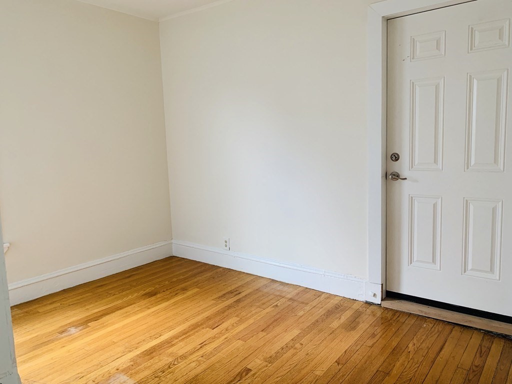 Empty room with polished hardwood floors and a white paneled door.