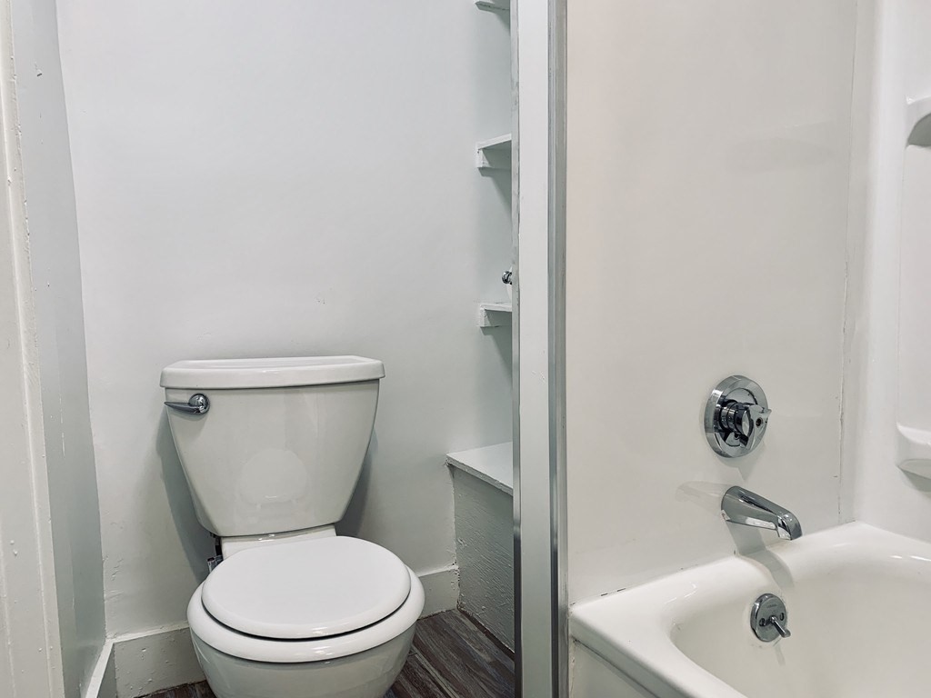 Bathroom with a white toilet beside a bathtub and shower enclosure, chrome fixtures, and dark flooring.