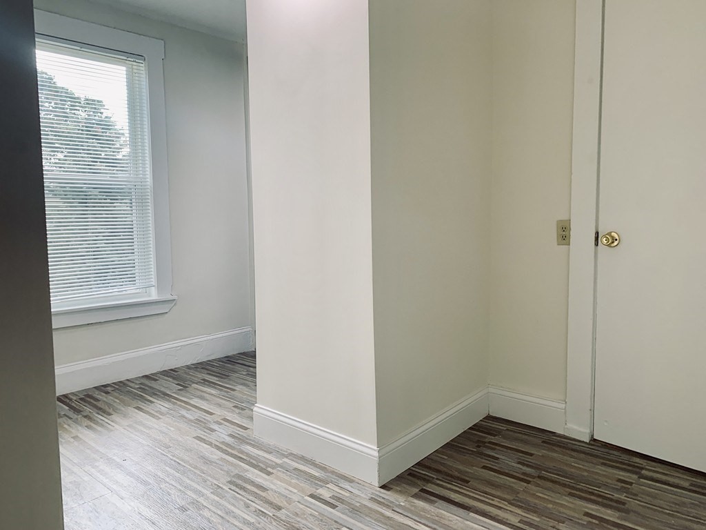 Empty room with a window, white blinds, and gray-brown patterned flooring.