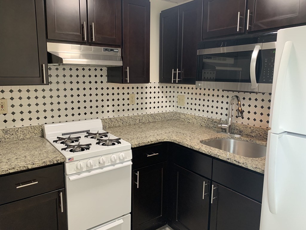 Kitchen with dark cabinets, granite counters, diamond-pattern backsplash, and white gas range.