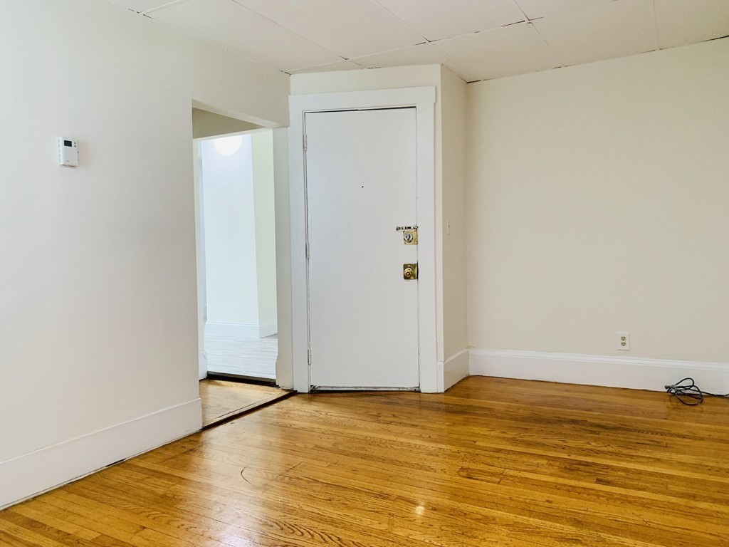 Unfurnished room with hardwood floors, a white entry door, and an open doorway to an adjoining room.
