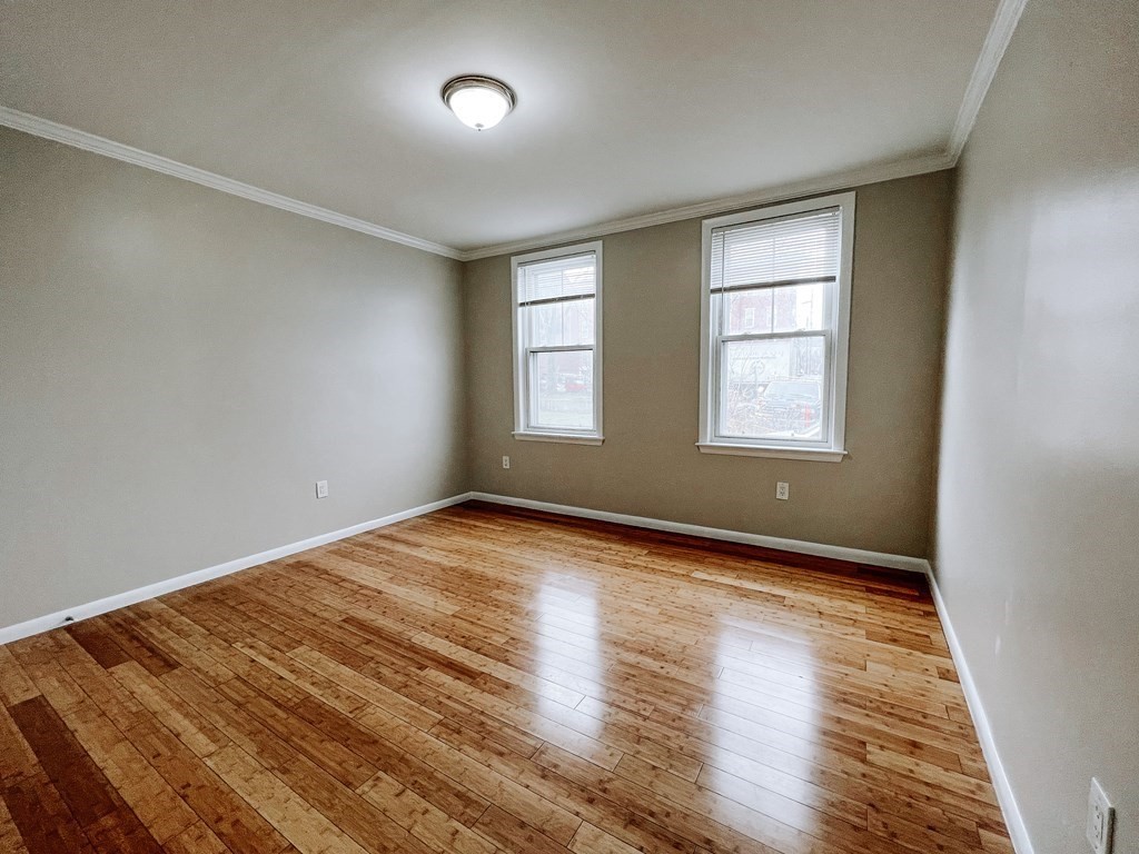 Empty bedroom with polished hardwood floors and two windows with blinds.