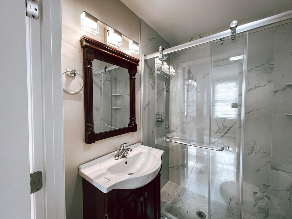 Bathroom with a dark wood vanity, framed mirror, and glass shower with marble-look tile.