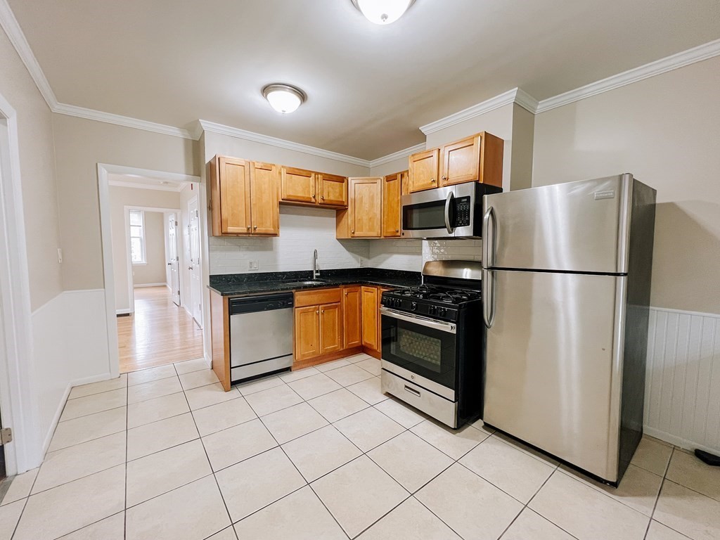 Kitchen with wood cabinets, black countertops, stainless steel appliances, and a light tiled floor.