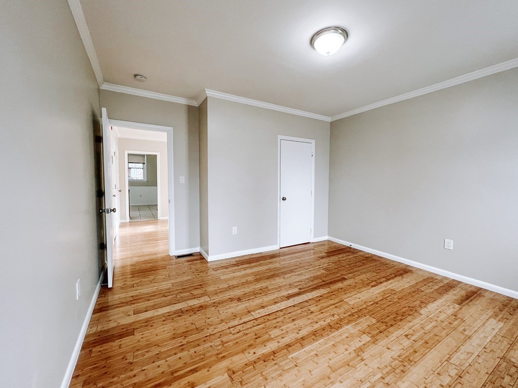 Empty room with polished hardwood floors, neutral walls, crown molding, and an open doorway.