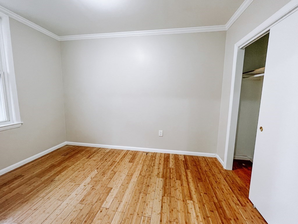 Empty bedroom with hardwood floors, a window, and an open closet.