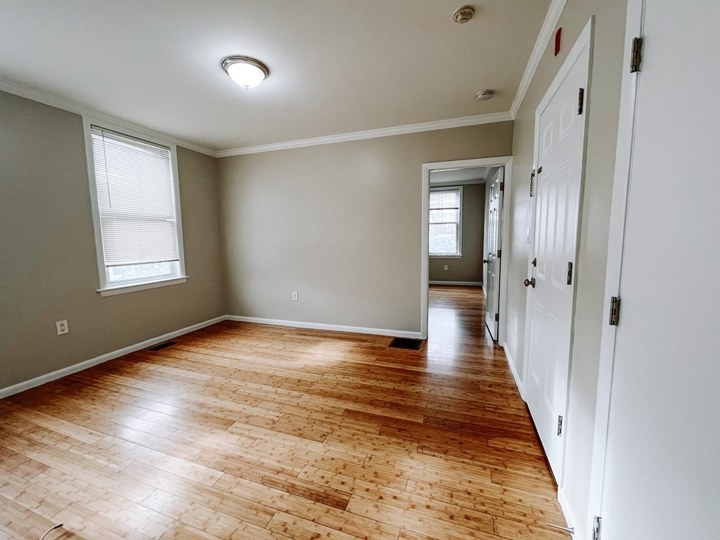 Empty room with polished hardwood floors, a window with blinds, and a doorway to another room.