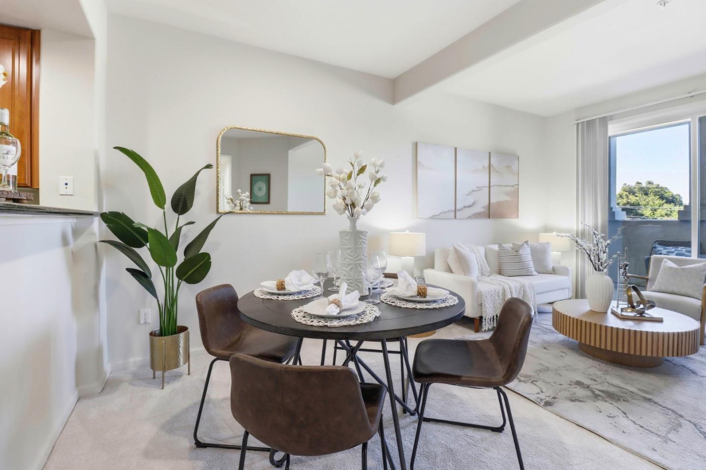 Staged dining and living area with a round table, white sofa, and sliding glass door to a balcony.
