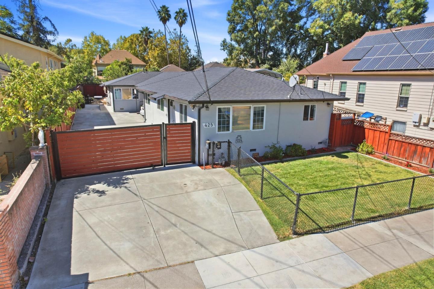 Single-story gray house with a wide gated driveway and fenced lawn.