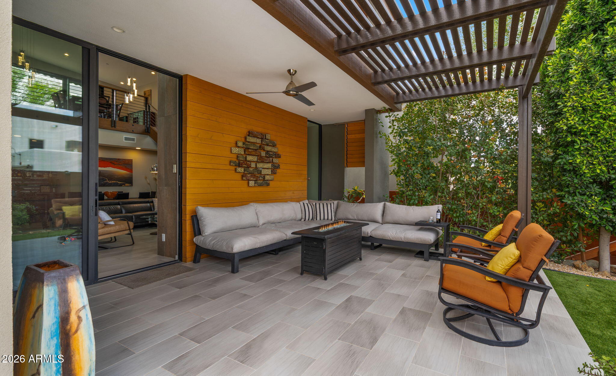 Modern patio with a wood pergola, gray sectional, orange chairs, and fire table.